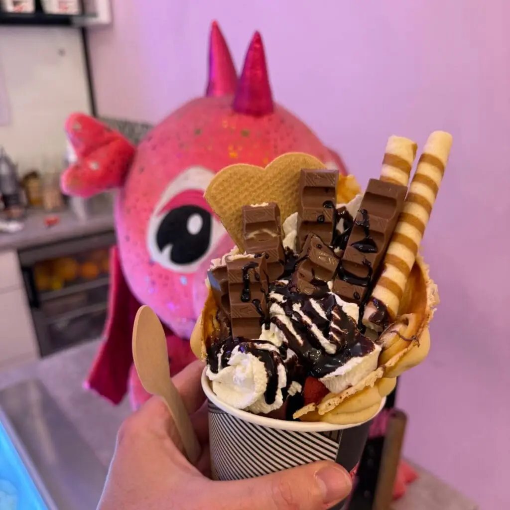 Postre helado en forma de gofre de burbujas con chocolate y nata montada, sostenido contra un dragón rosa en la heladería Smocza Gała de Cracovia (Polonia).