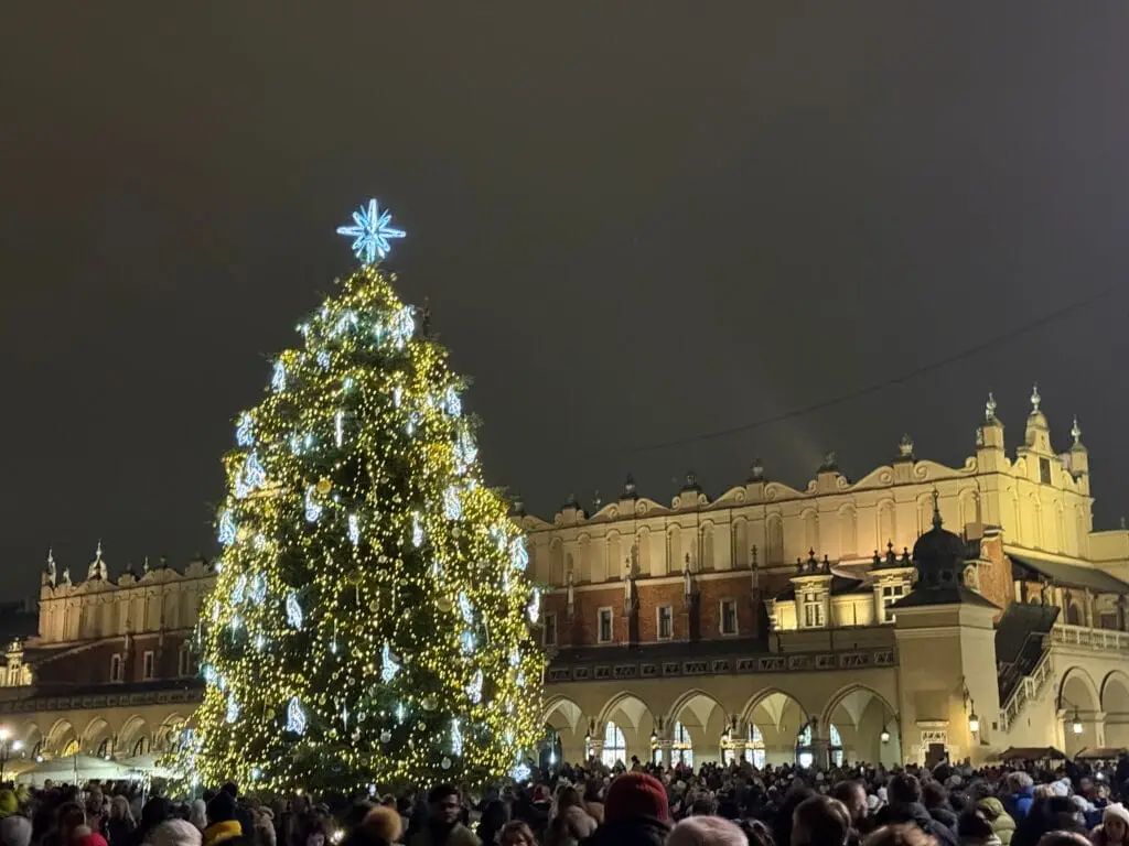 Christmas in Krakow - illuminated Christmas tree on the Main Square in front of the Cloth Hall, crowds of people in the evening
