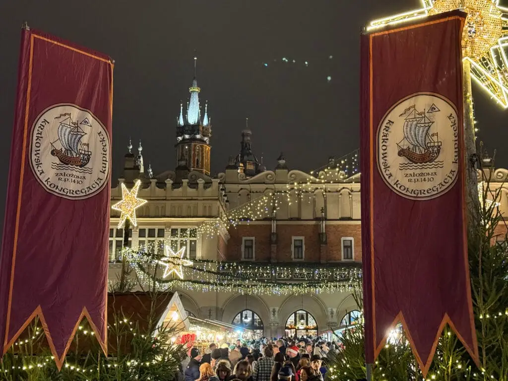 Christmas in Krakow - banners of the Krakow Merchant Congregation against the background of the Cloth Hall, Christmas lights and a crowd at the Christmas market