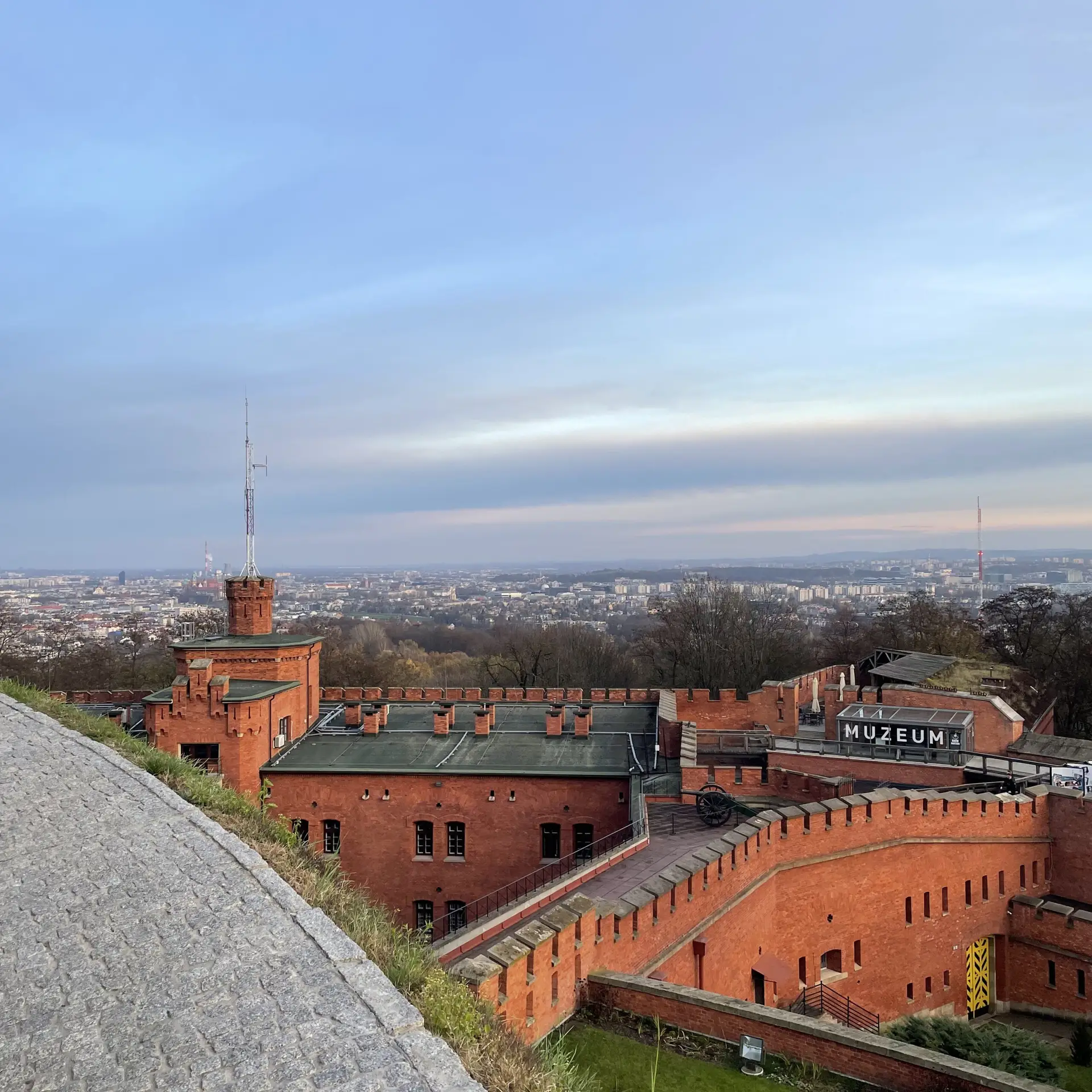 Vista aérea del Fuerte Kościuszko en Cracovia, con sus murallas defensivas de ladrillo y la inscripción del museo, con el panorama de la ciudad como telón de fondo.
