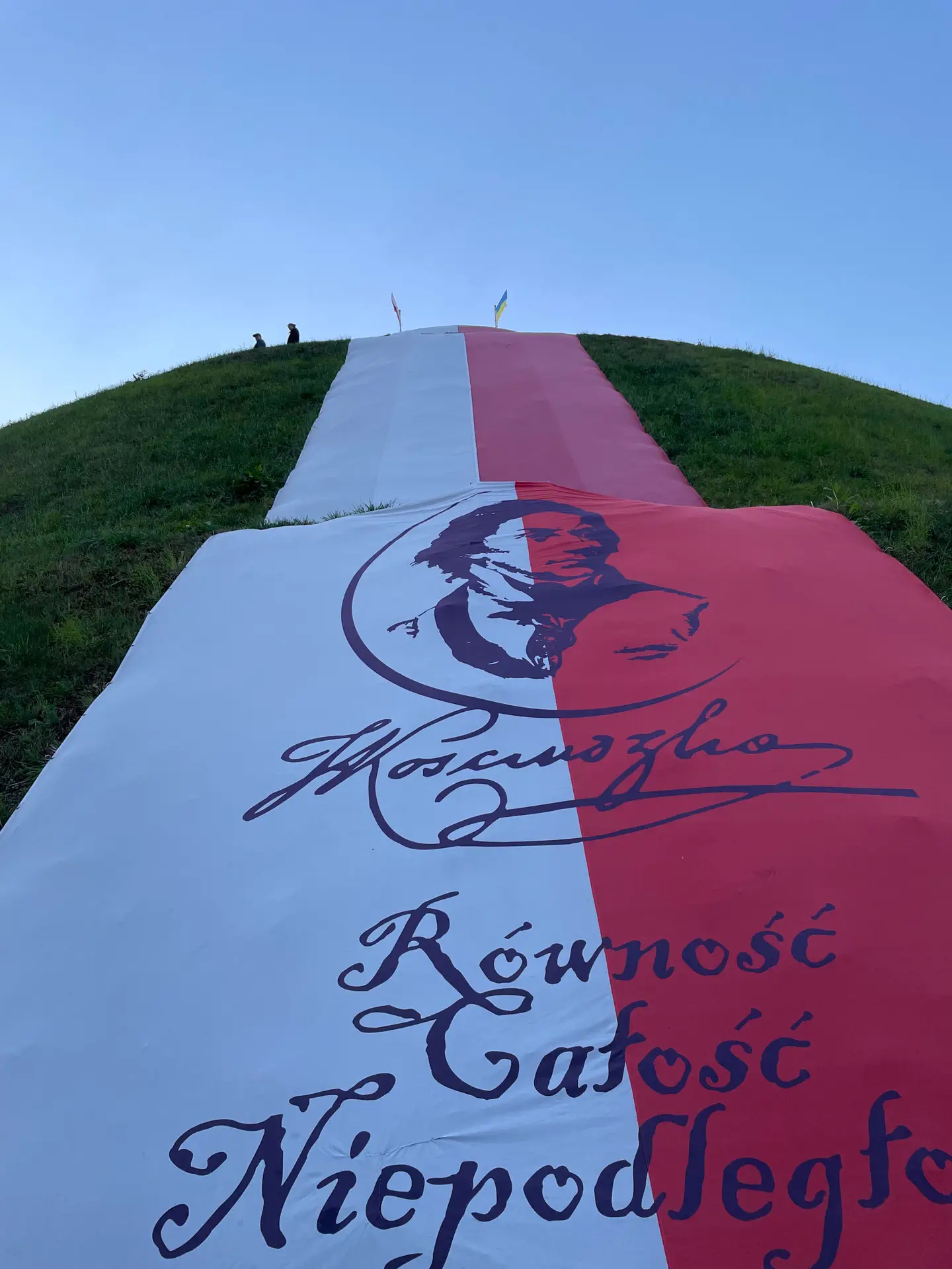 Una bandera blanca y roja con un retrato de Tadeusz Kościuszko y los lemas "Igualdad, Integridad, Independencia" ondeaba en la ladera del túmulo de Kościuszko.